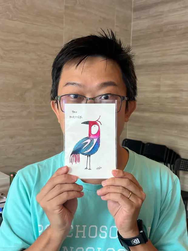 A man holding his finished painting of a wading bird up beside his face