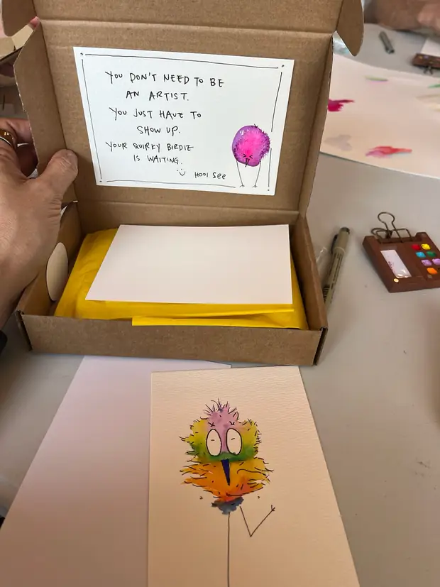An open kraft box with a hand-lettered note reading you don't need to be an artist, you just need to show up